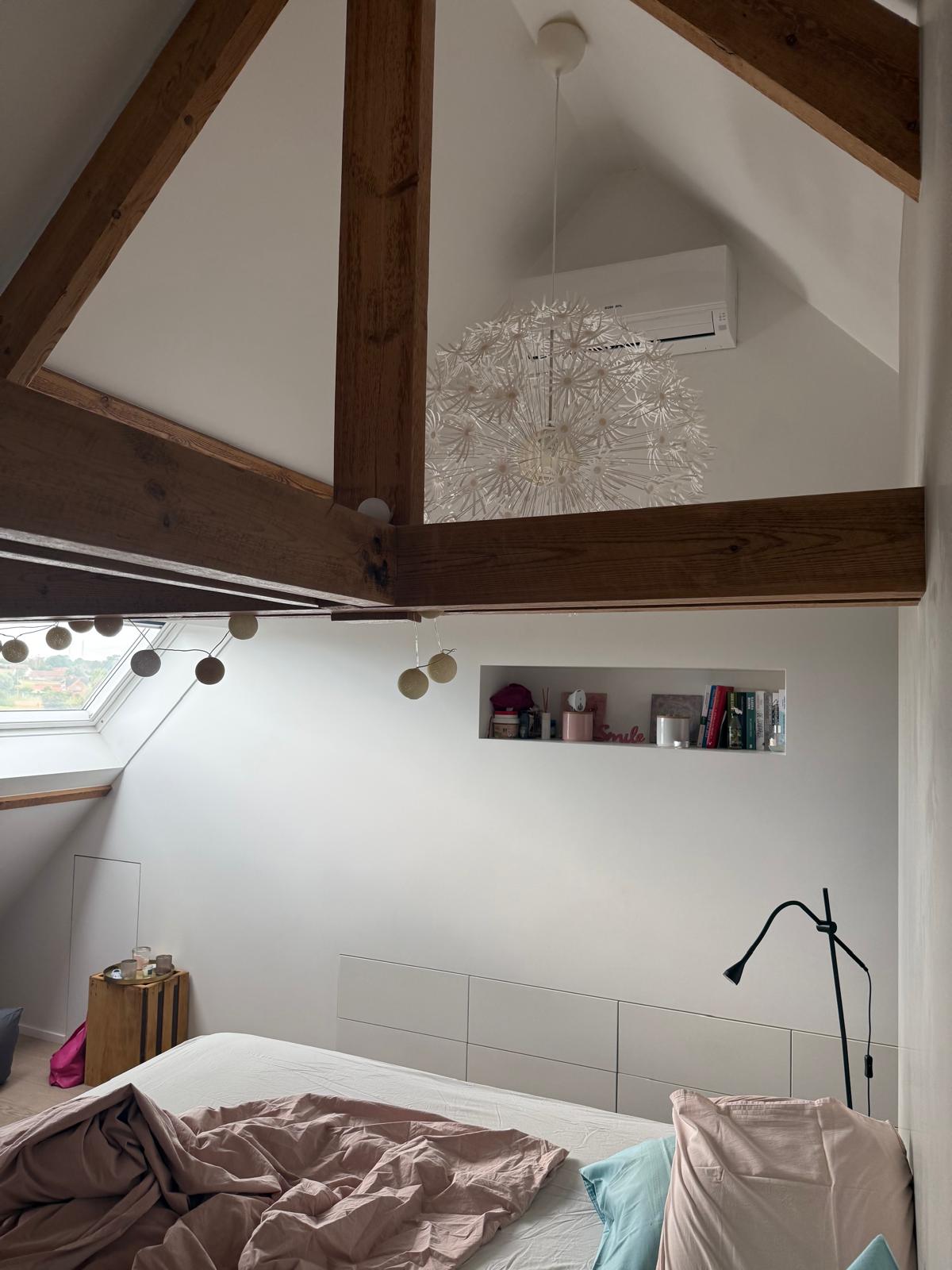 Binnenunit van de airco tegen de topgevel onder de houten dakspanten in de ouderslaapkamer in Elsegem