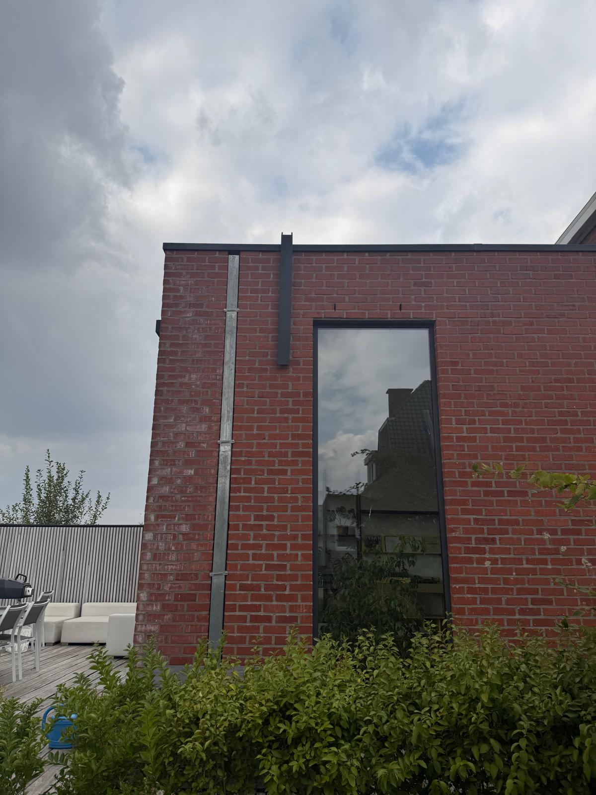 Strakke bakstenen gevel van de woning in Elsegem waar het leidingtraject van de airco discreet is weggewerkt