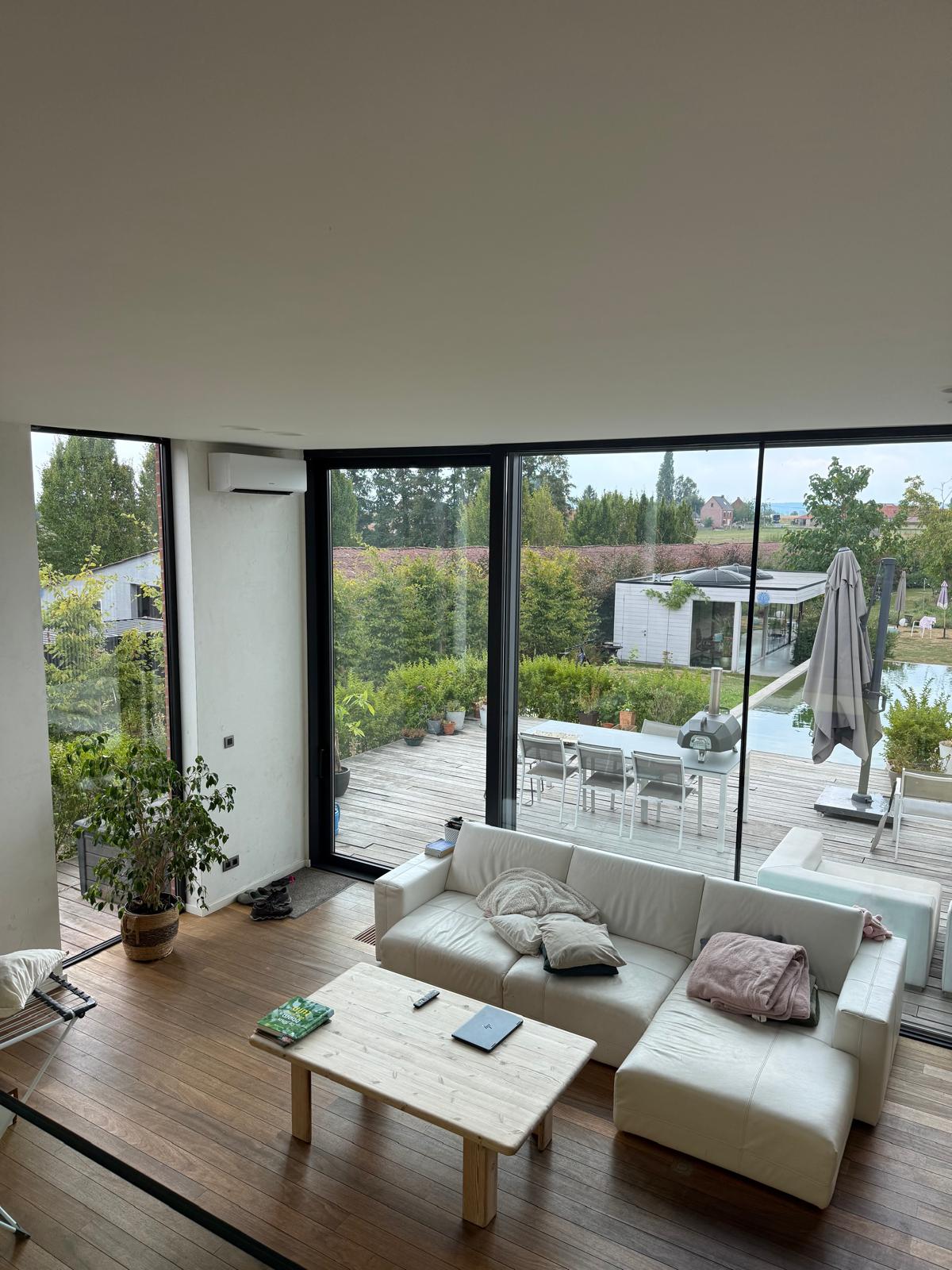 Binnenunit van de airco in de lichte leefruimte met grote glaspartijen van de woning in Elsegem